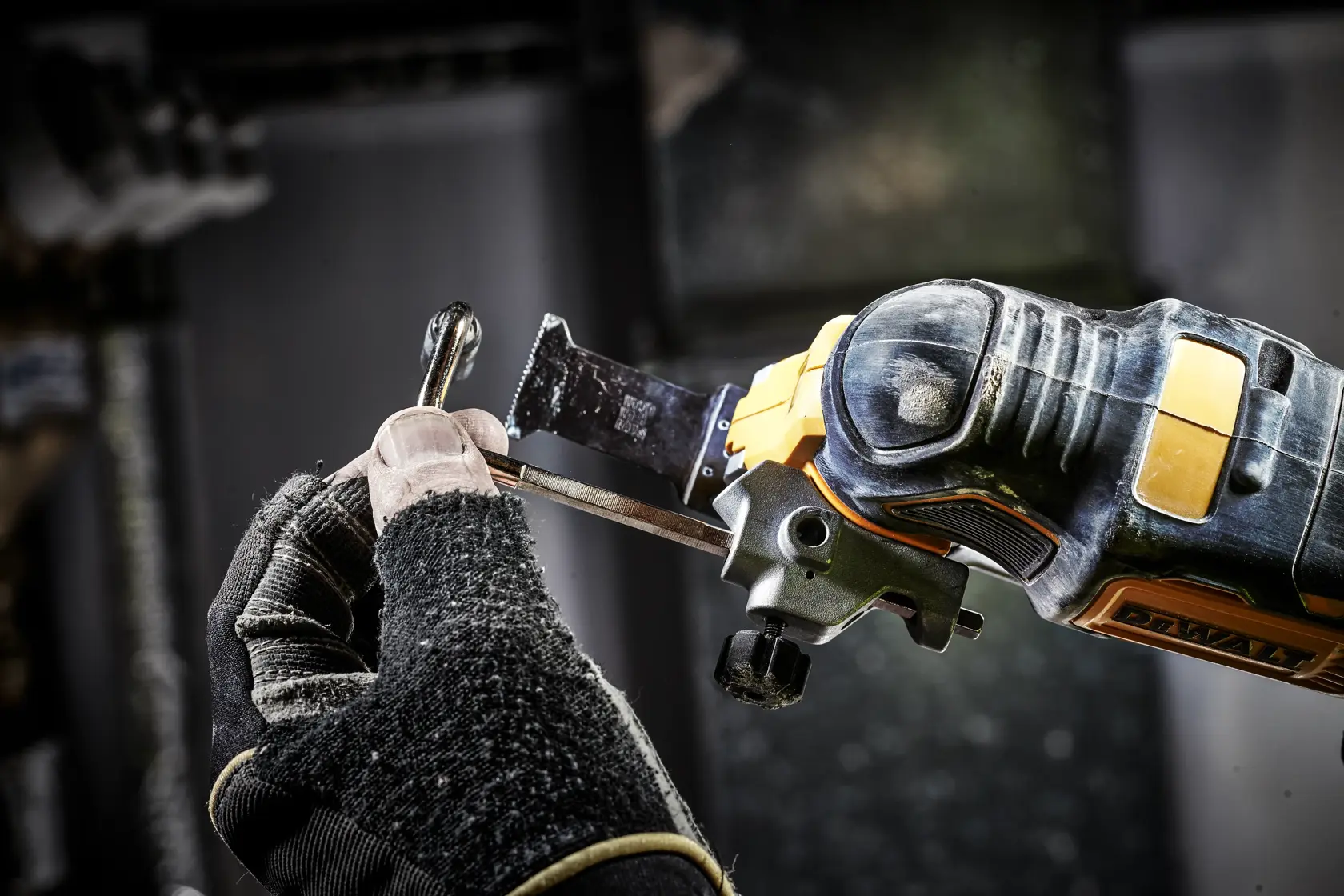 Gloved hand uses a DEWALT oscillating tool to cut metal in a workshop.