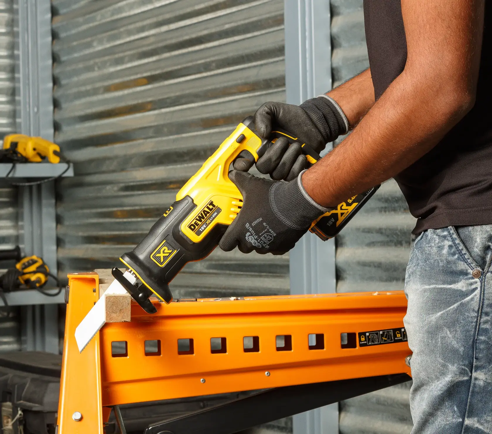 Person uses DEWALT DCS367P2 reciprocating saw to cut wood on an orange metal workbench in a workshop.