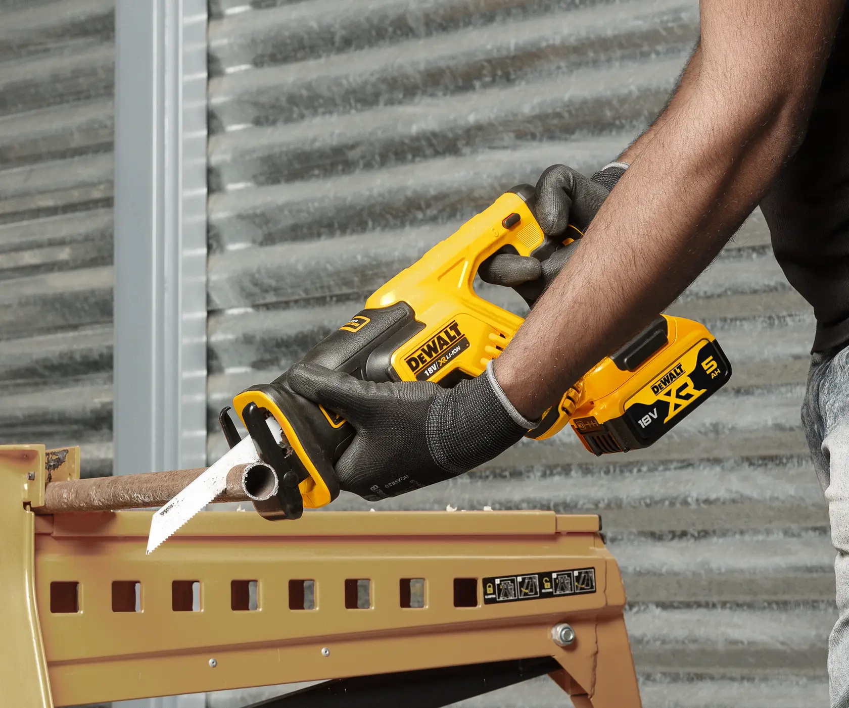 Person using a DEWALT cordless reciprocating saw to cut a metal pipe while wearing gloves.