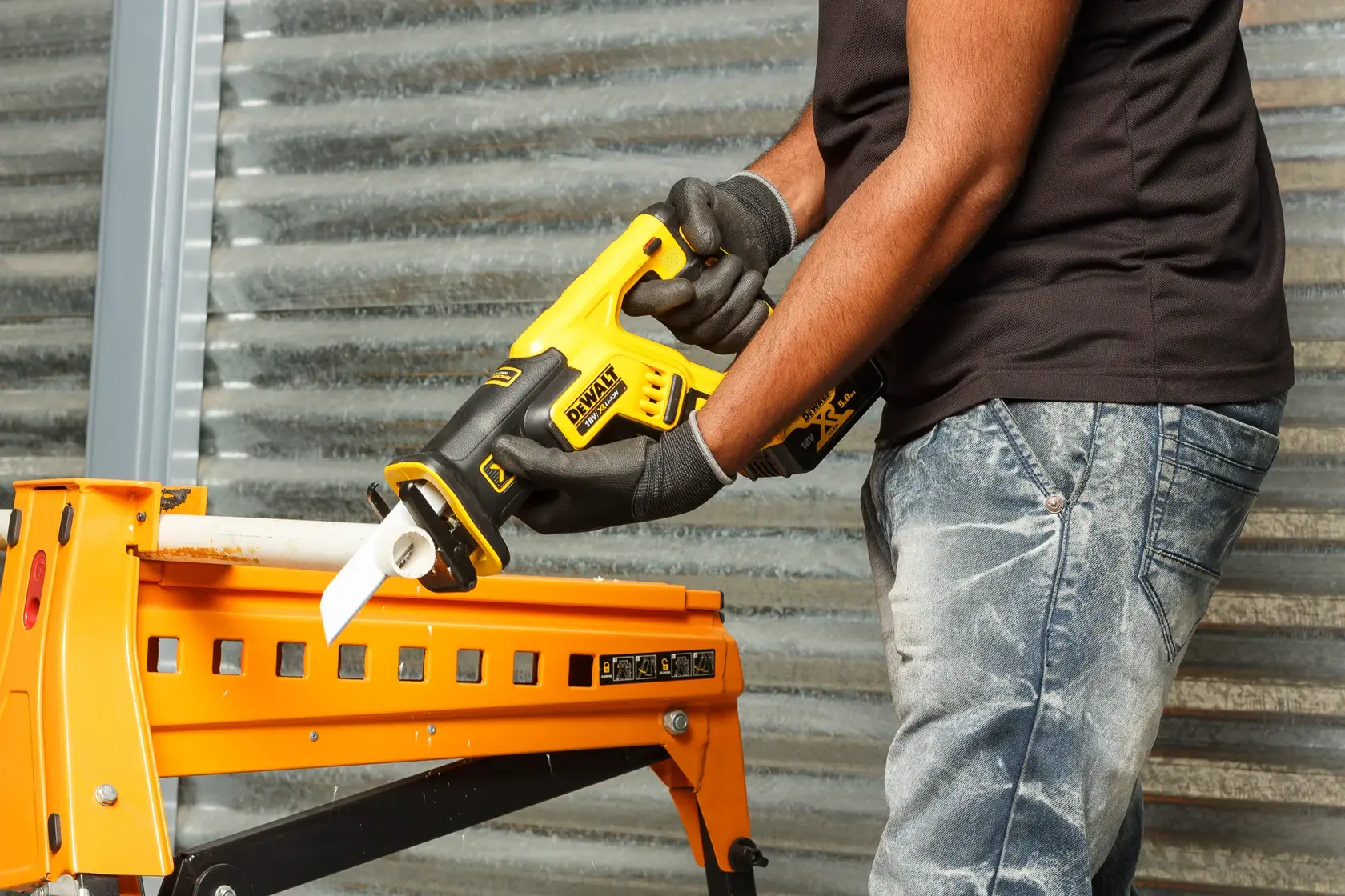 Person using DEWALT DCS367P2 saw to cut a pipe held on a yellow workbench indoors.