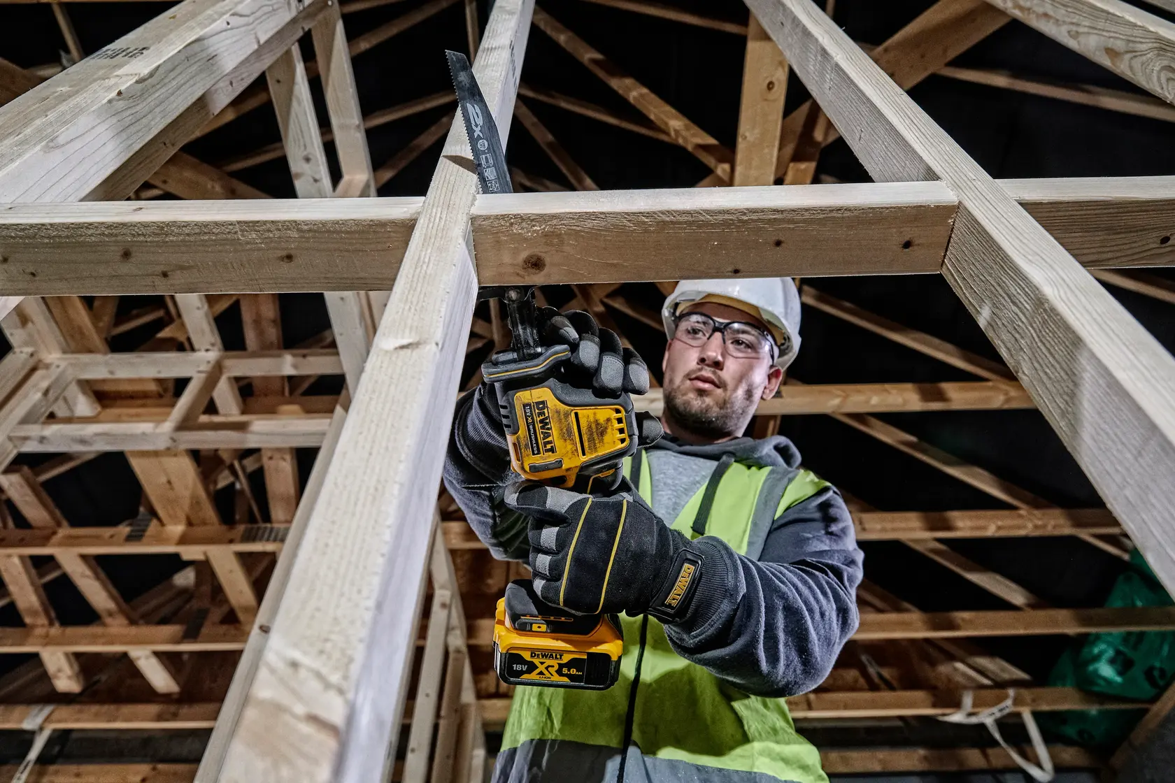 Photo of DEWALT DCS369P2 cordless reciprocating saw used on wood frame construction by a worker wearing safety gear.