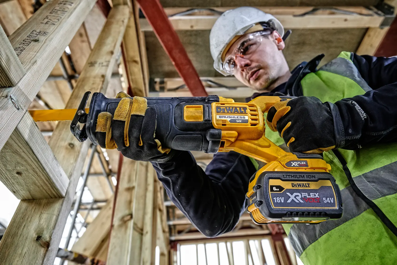 Worker using DEWALT DCS389T2 cordless reciprocating saw on wood frame at construction site.