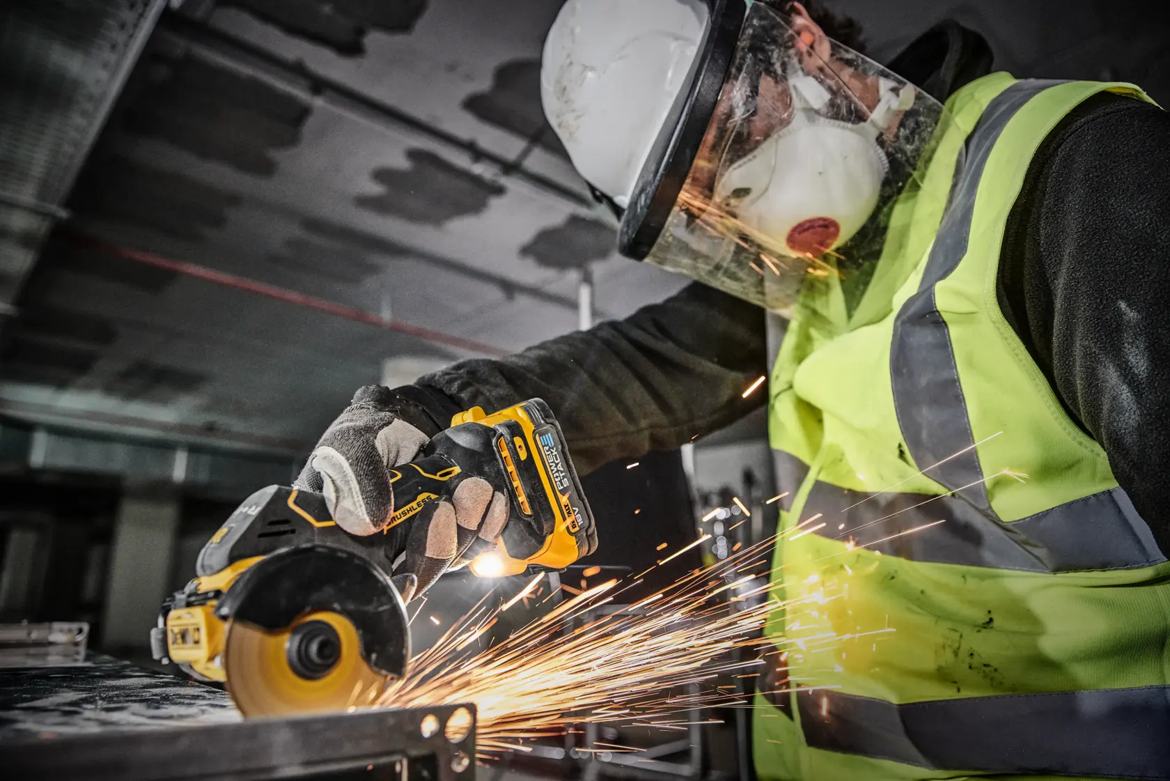 A person wearing safety gear, including a helmet, face shield, mask, gloves, and a high-visibility vest, is using a DEWALT cordless metal cutting tool, generating sparks while working on a metal surface in an industrial environment.