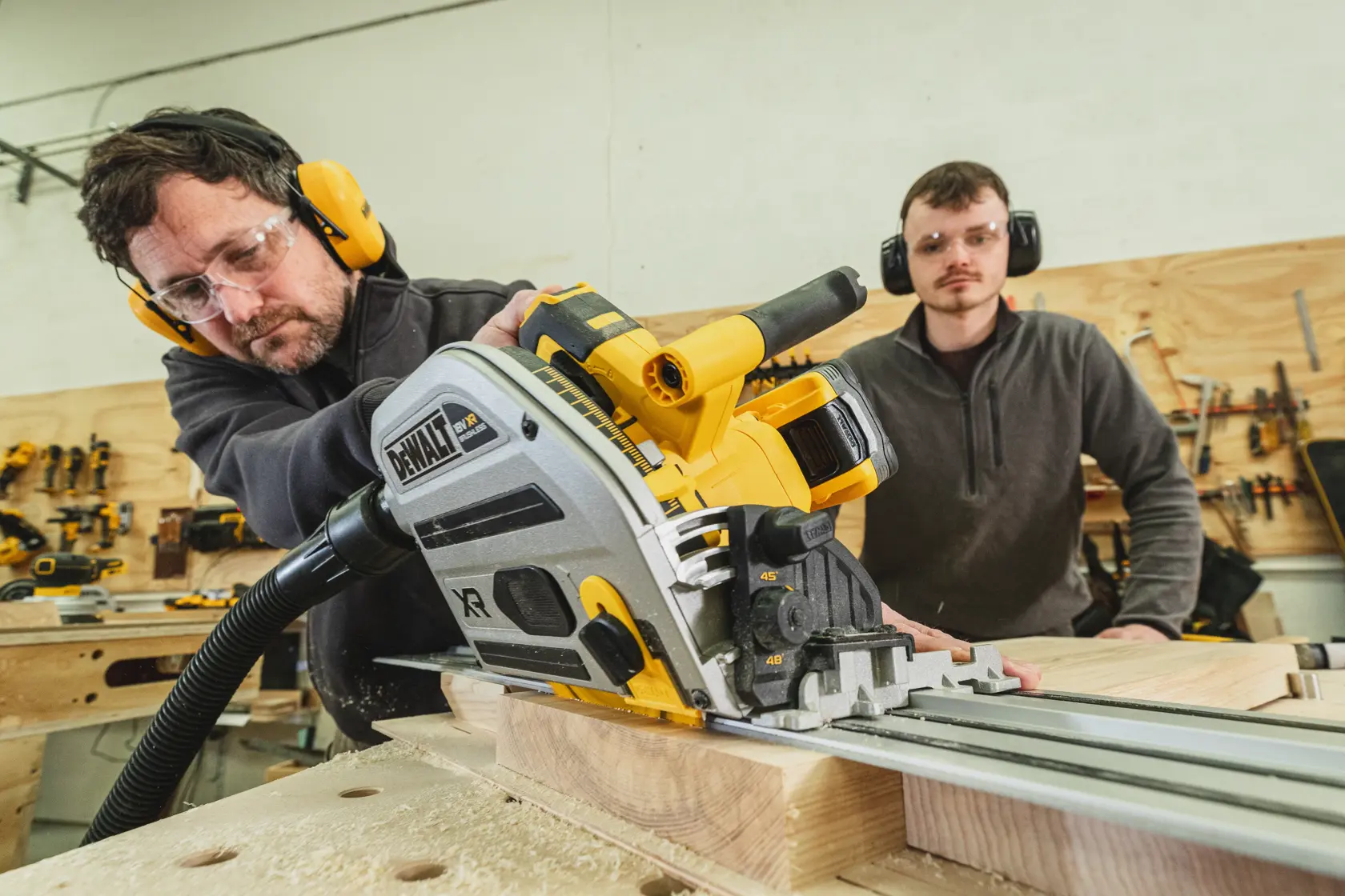 Man using a DEWALT track saw to cut wood, with another person observing in a workshop.