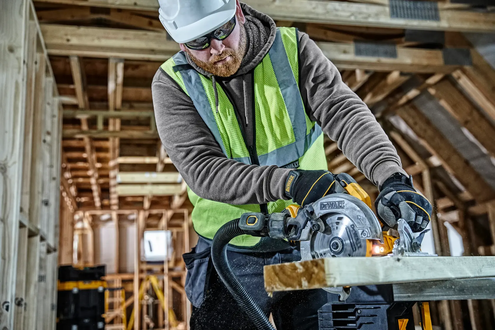 Worker uses DEWALT DCS570 circular saw to cut wood in a construction area. Safety gear and gloves are worn.