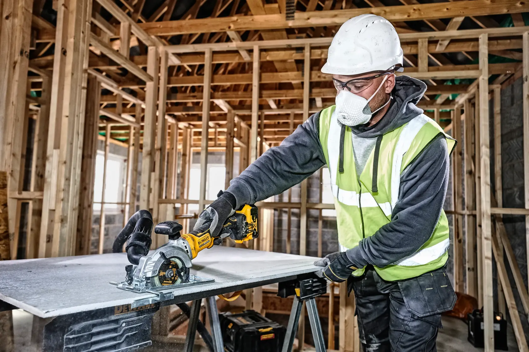 Worker uses DEWALT cordless circular saw to cut material at a construction site, wearing safety gear.