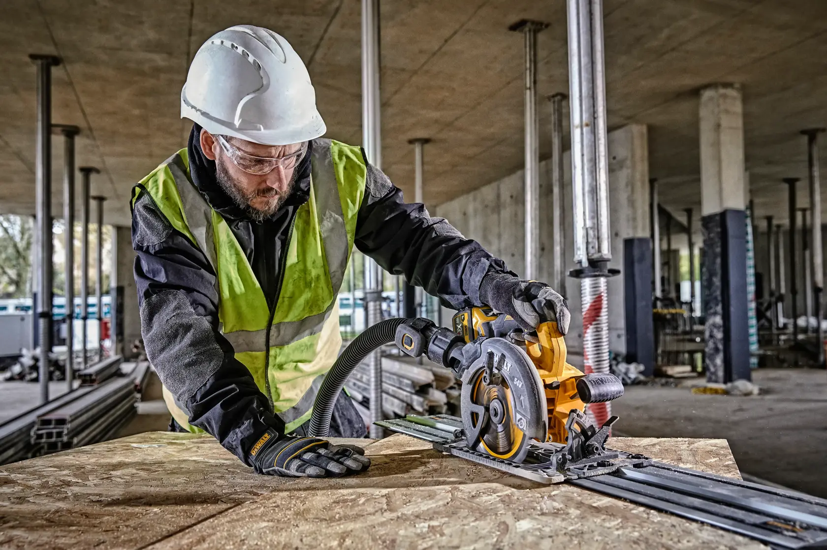 Worker uses a DEWALT circular saw to cut wood on a construction site, wearing safety gear and gloves.