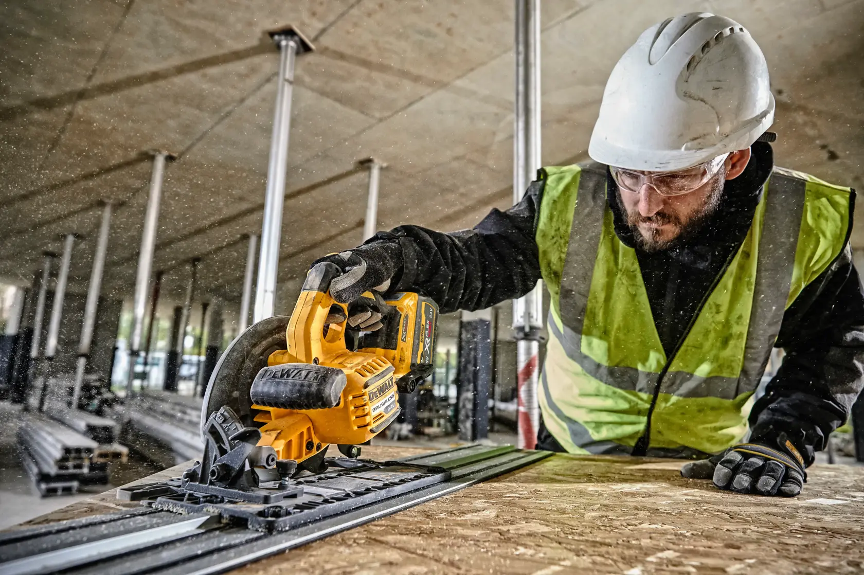 Worker uses DEWALT cordless circular saw, wearing safety gear, cutting wood at construction site indoors.