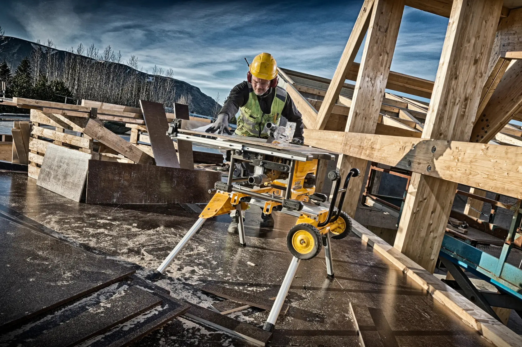 Worker uses DEWALT DCS7485N table saw on construction site with wooden beams and safety gear.