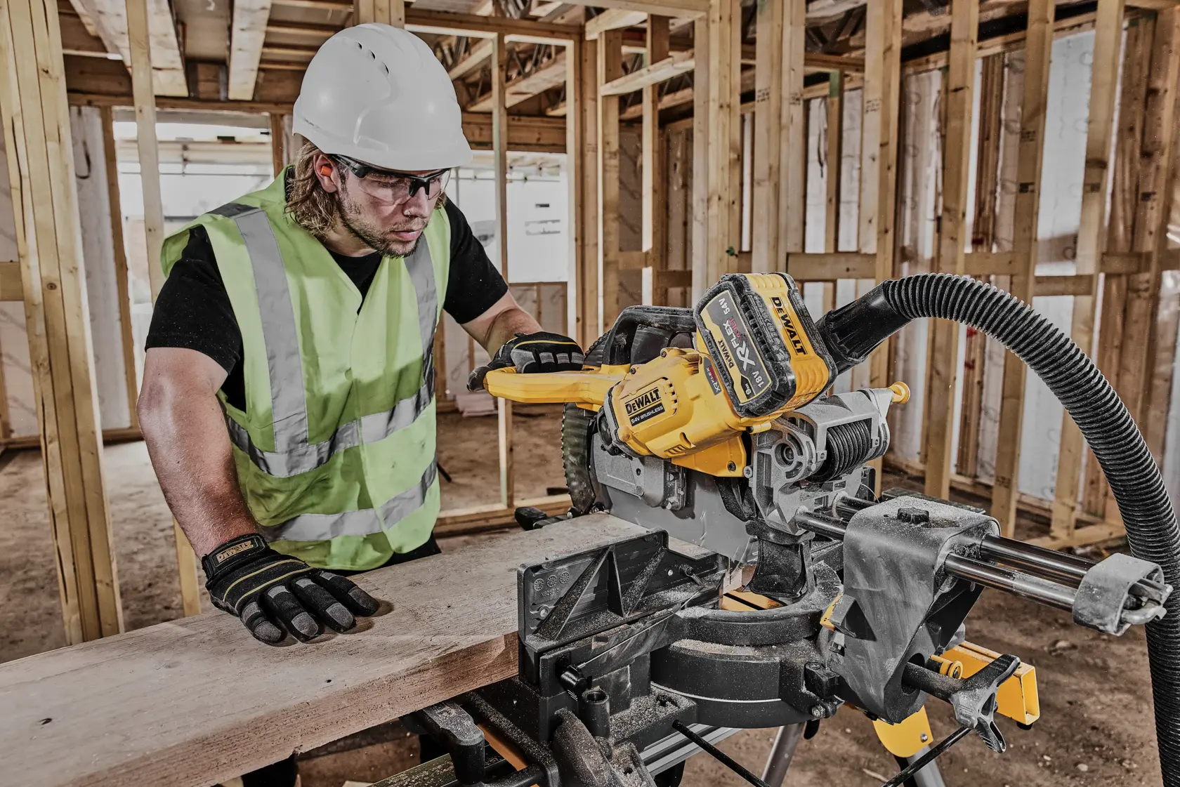 Worker uses DEWALT DCS781N saw to cut wood at a construction site. Safety gear and reflective vest worn.