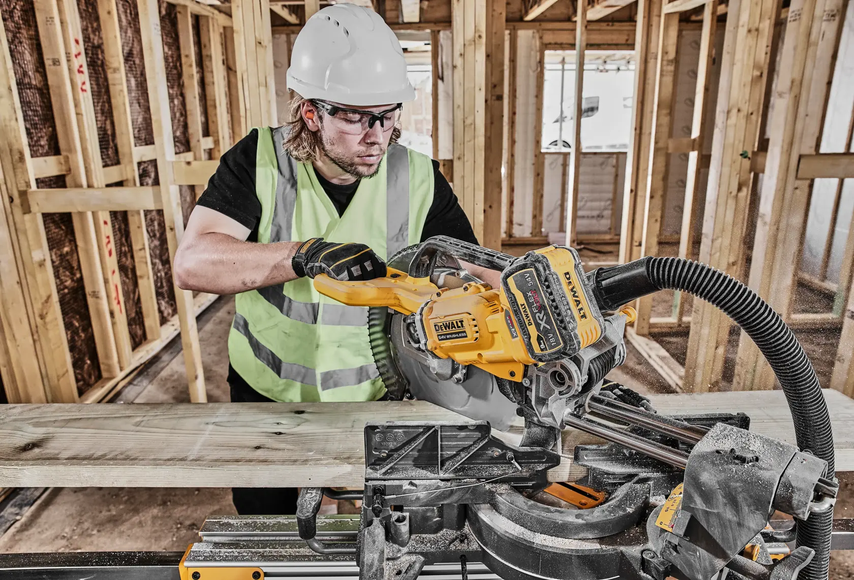 Worker using a DEWALT DCS781N saw to cut wooden planks at a construction site while wearing safety gear.
