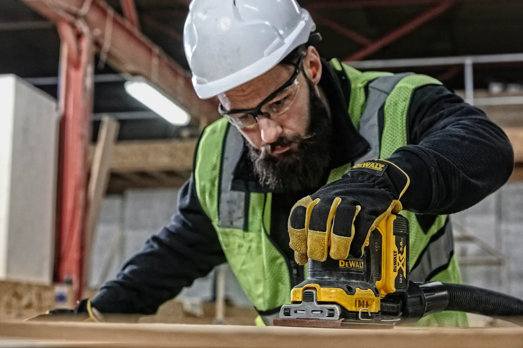 Worker uses DEWALT DCW200N sander on wood, wearing safety gear and gloves at construction site.