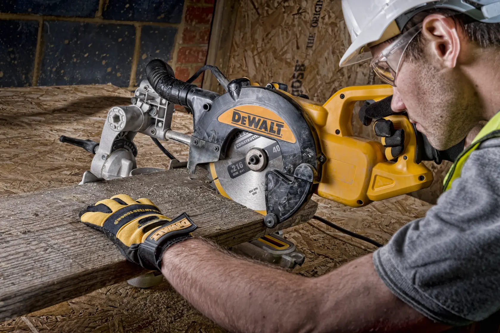 DEWALT miter saw cutting wood, operated by person wearing gloves and helmet at construction site.