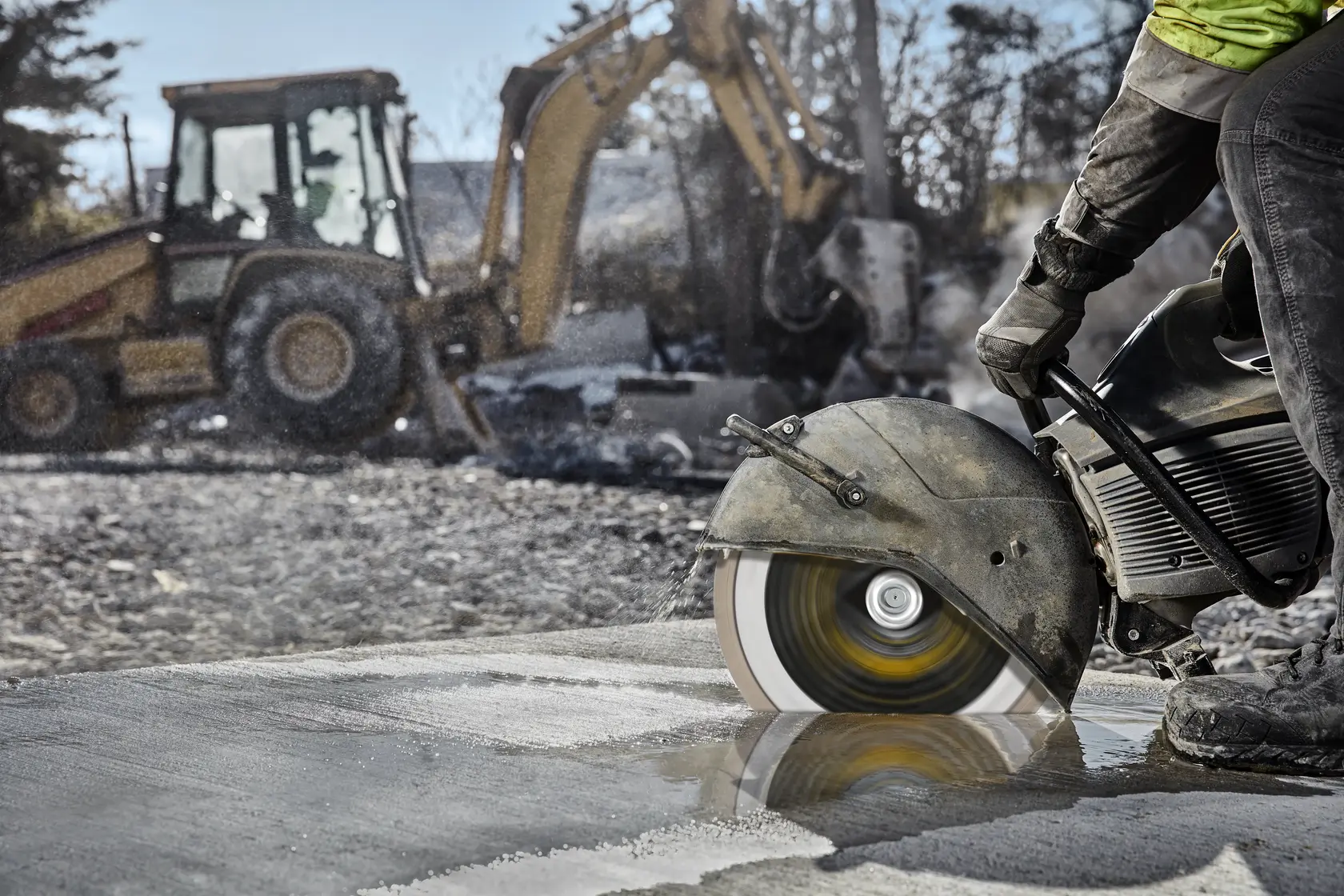 A DEWALT saw with DT20462 blade cuts concrete on a construction site. Heavy machinery is visible in the background.