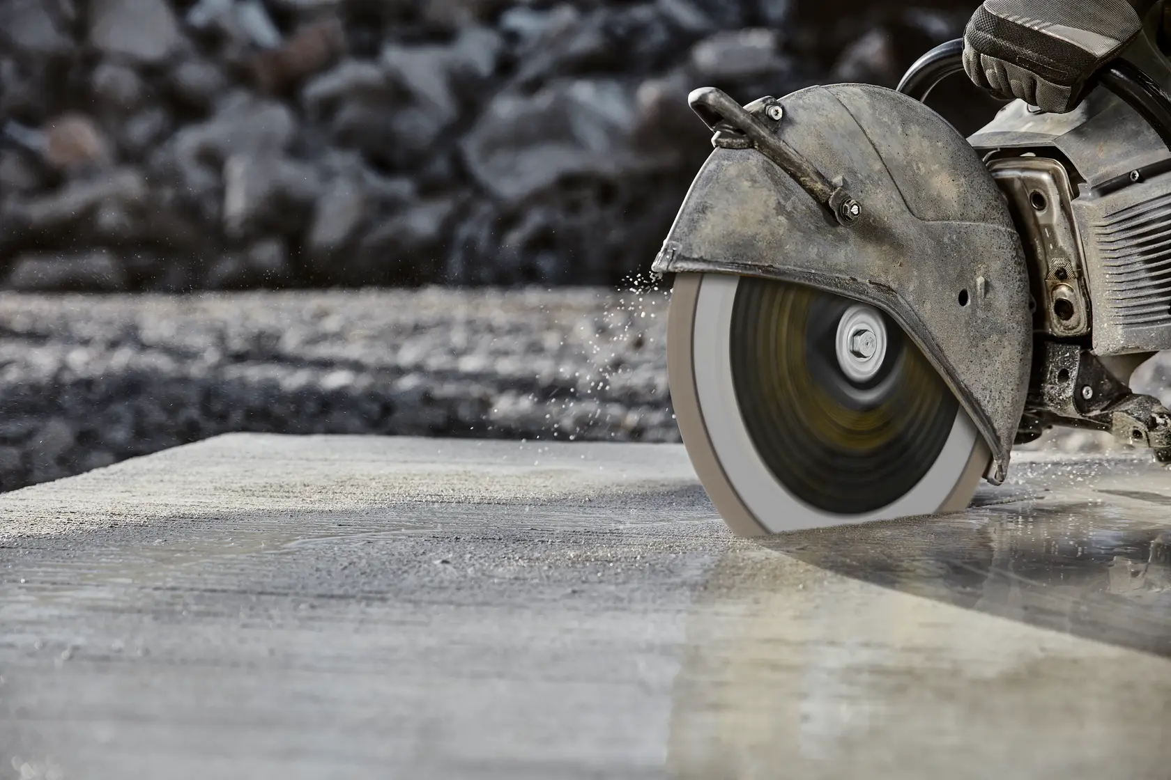 A close-up of a power saw cutting through wet concrete outdoors, water splashing from the blade.