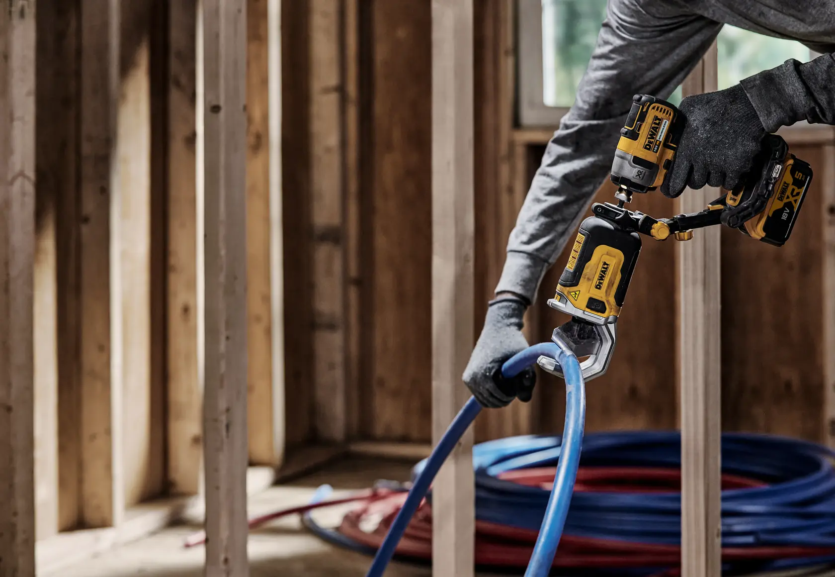 DEWALT tool in use, cutting a blue pipe in a construction site with wooden framing and coiled pipes visible.