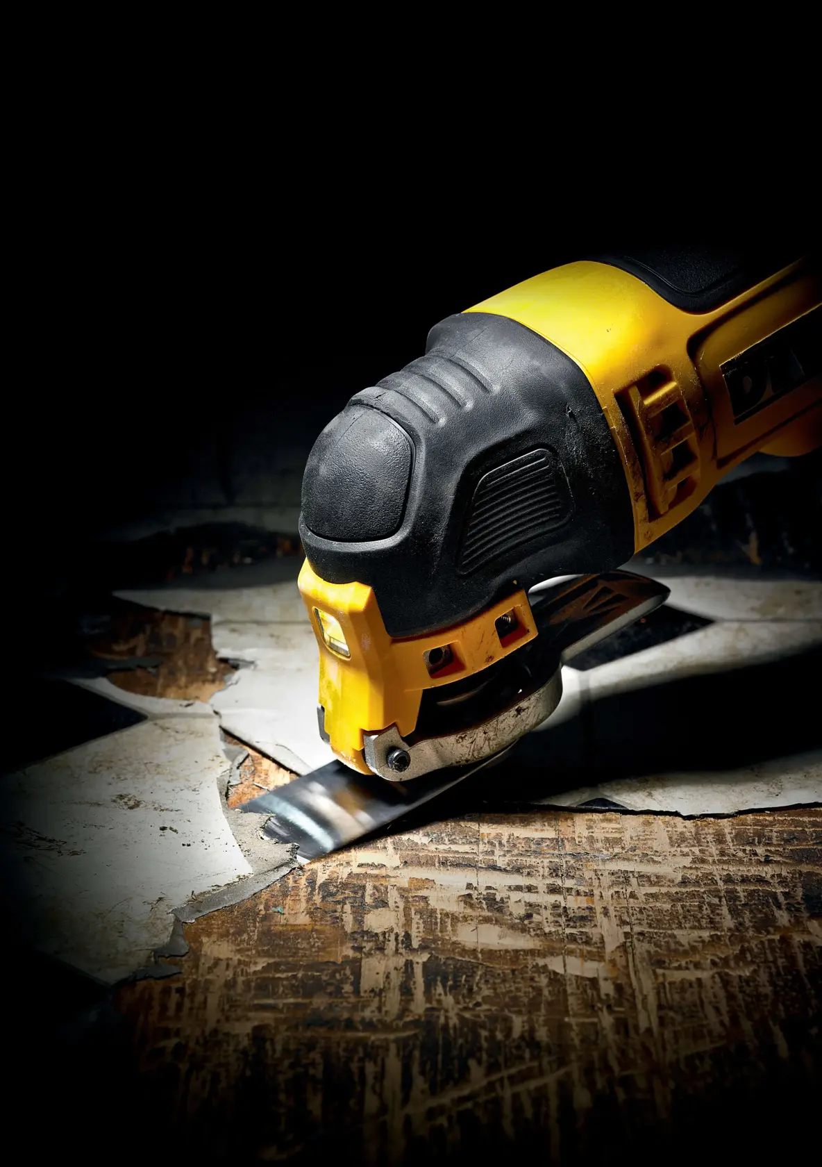 DEWALT oscillating multi-tool cutting through old flooring in a close-up, showing tool detail and action.