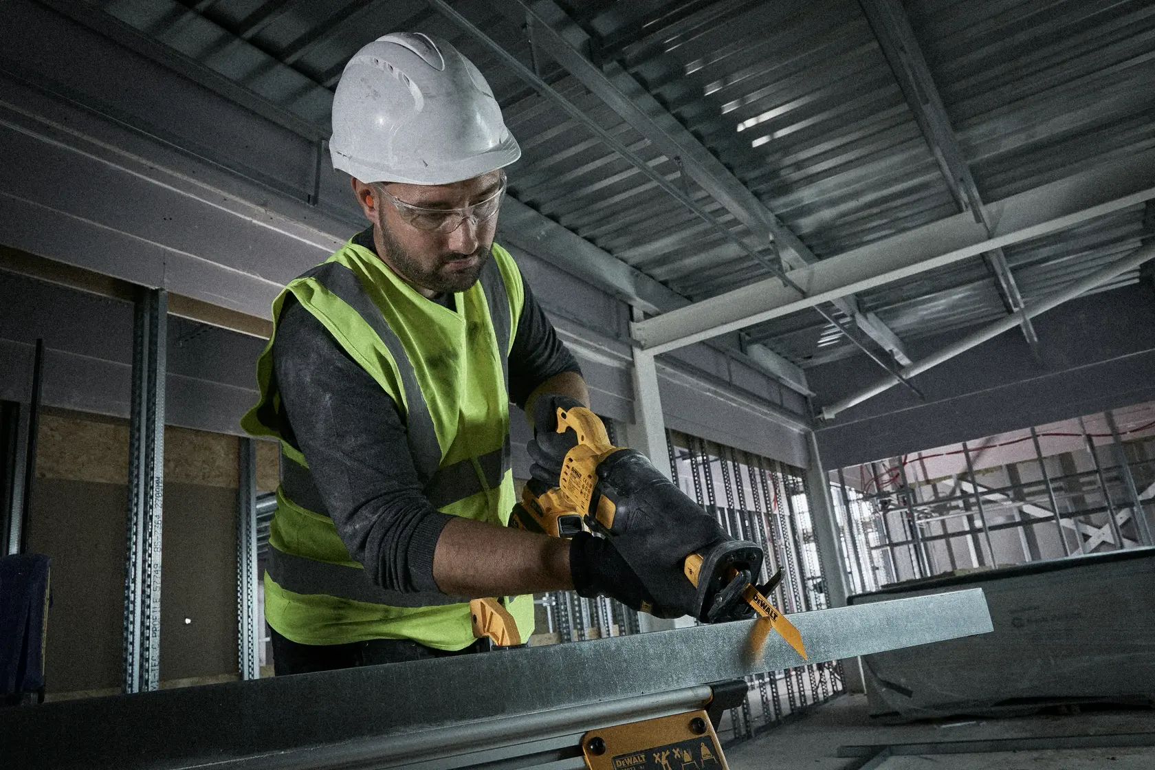 Worker using a yellow DEWALT saw to cut metal in an industrial setting, wearing safety gear and gloves.