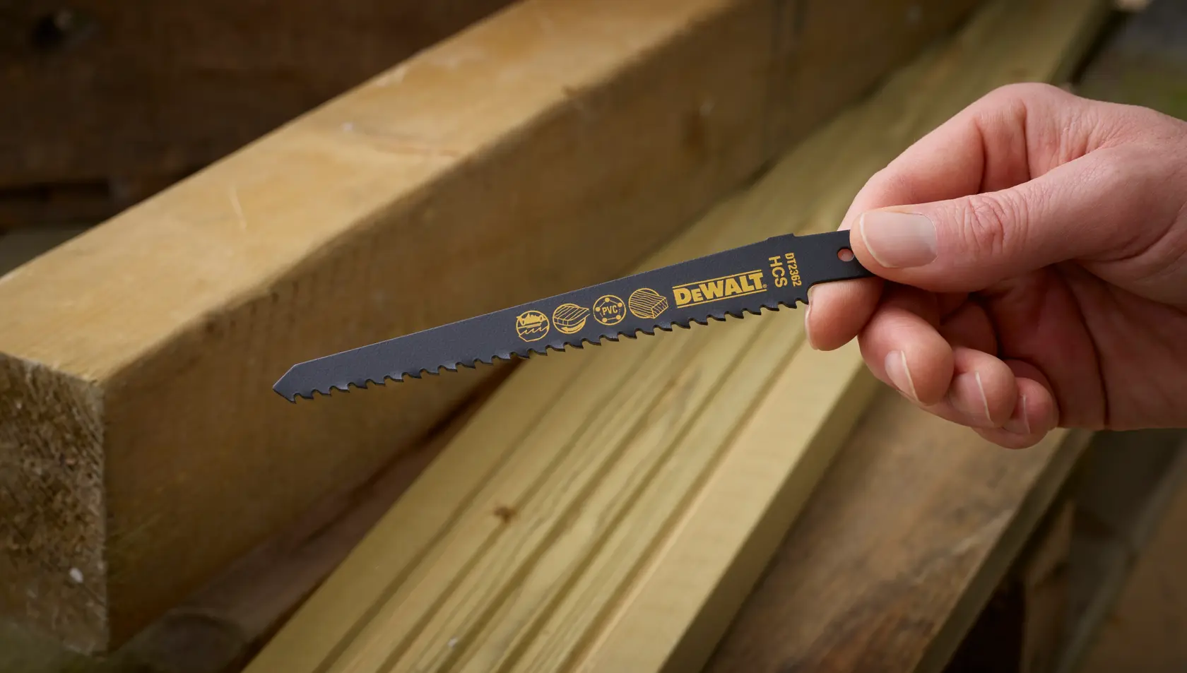 Hand holding a DEWALT DT2362 saw blade, placed near wooden planks in a workshop setting.