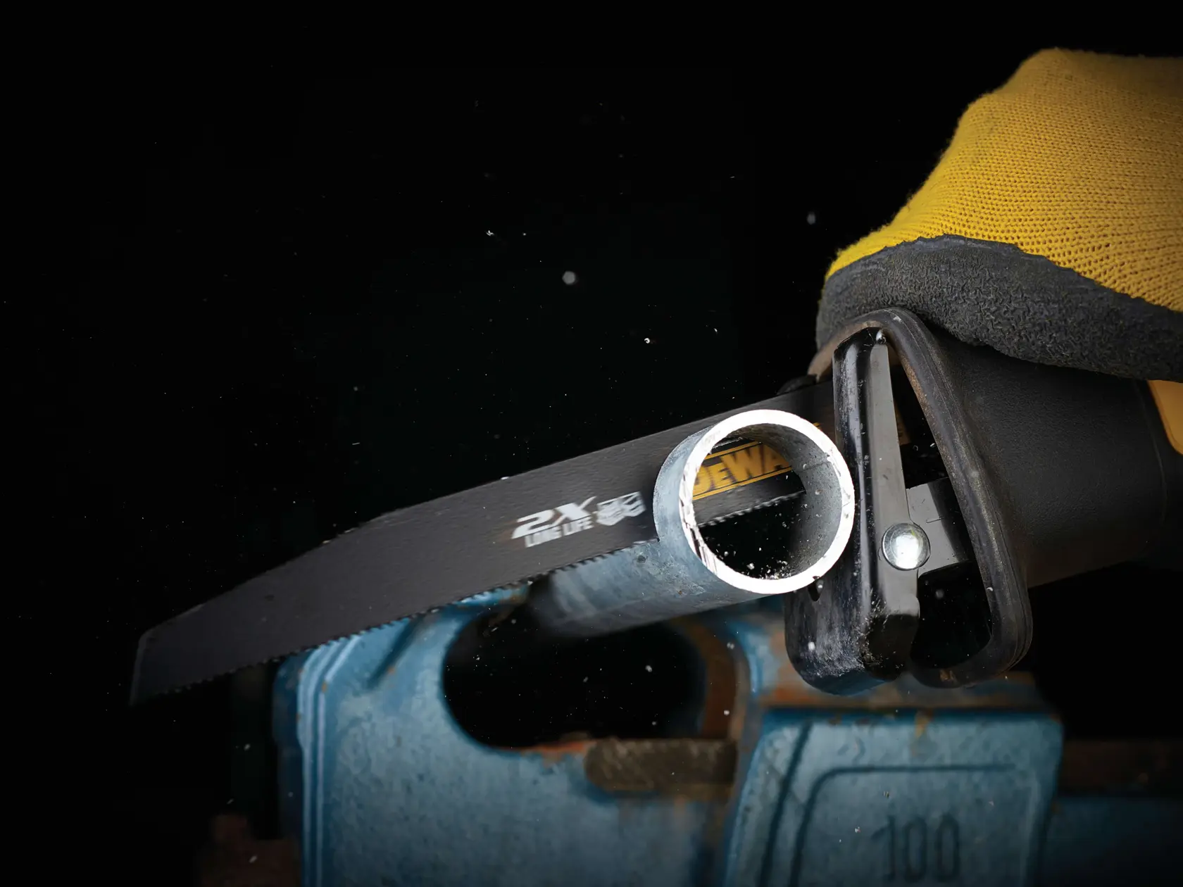 DEWALT saw blade cutting through a metal pipe held in a vise, with a gloved hand operating the tool.