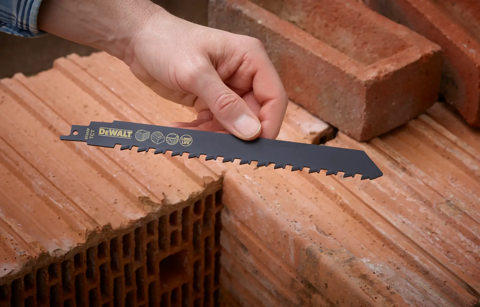 Hand holding a DEWALT DT2420 saw blade above stacked bricks, showcasing its use for masonry cutting.