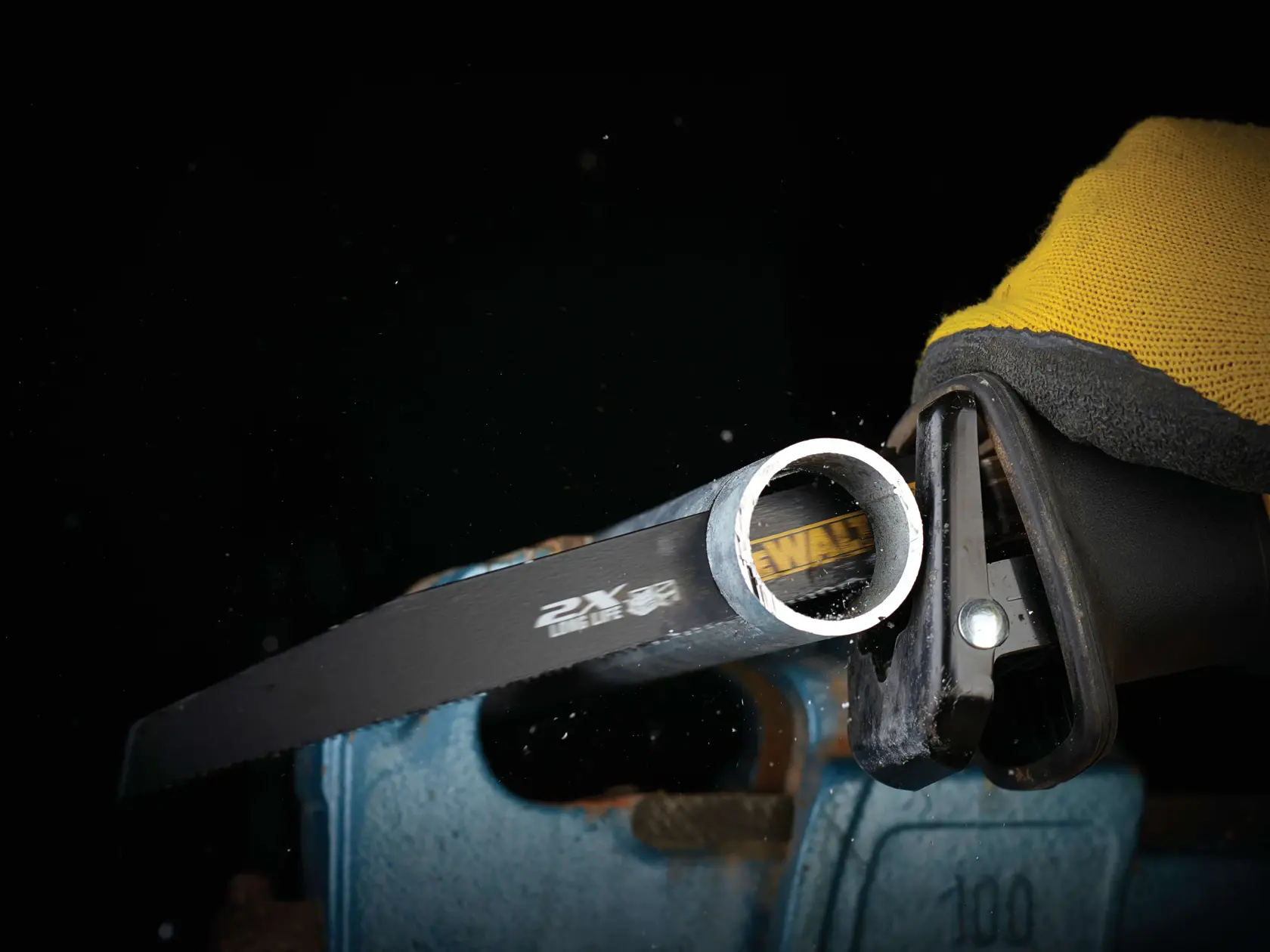Close-up of a DEWALT saw blade cutting through a metal pipe using a power tool, glove visible.