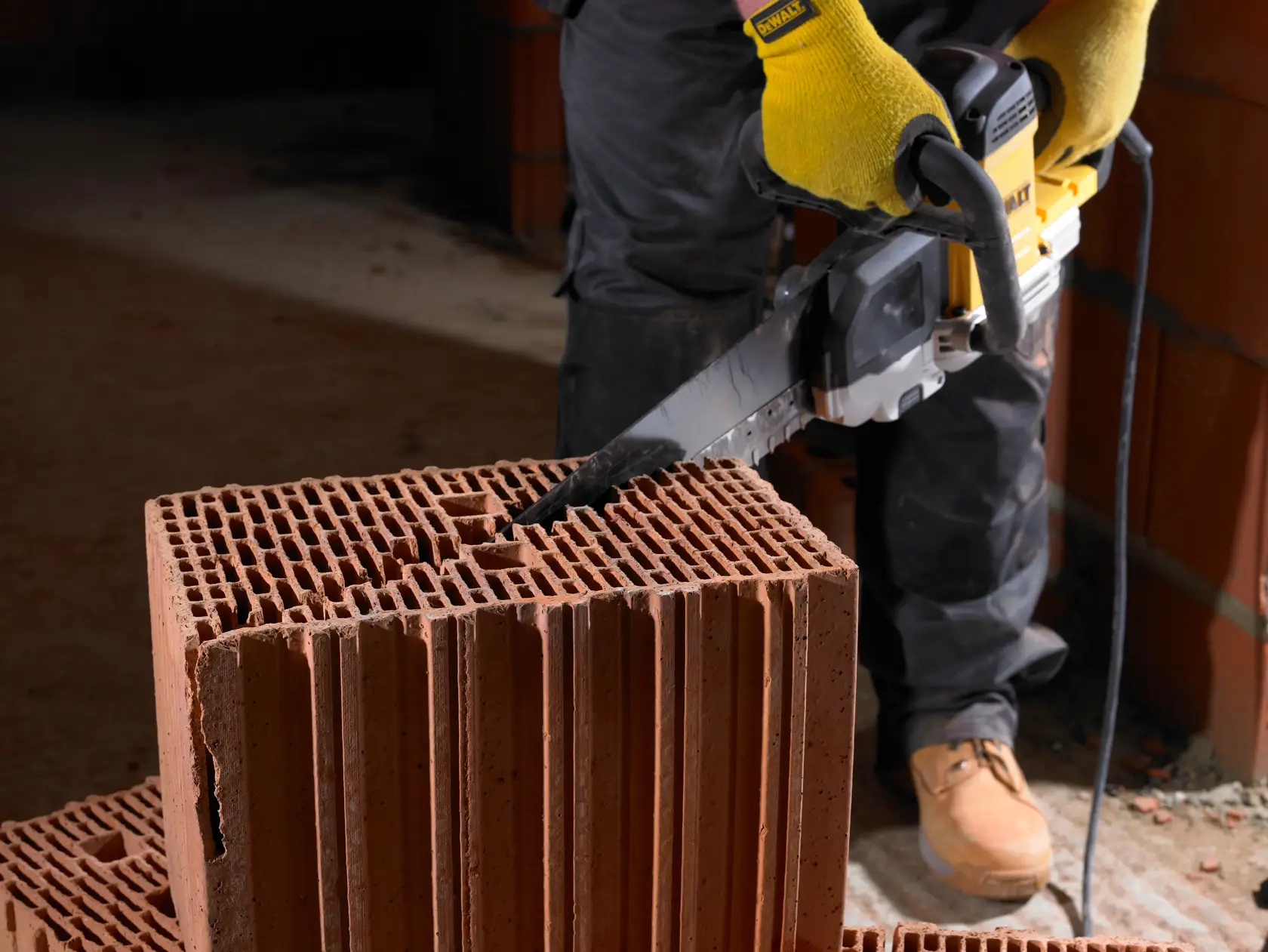 Person using a DEWALT saw to cut through a hollow construction brick in a work area.