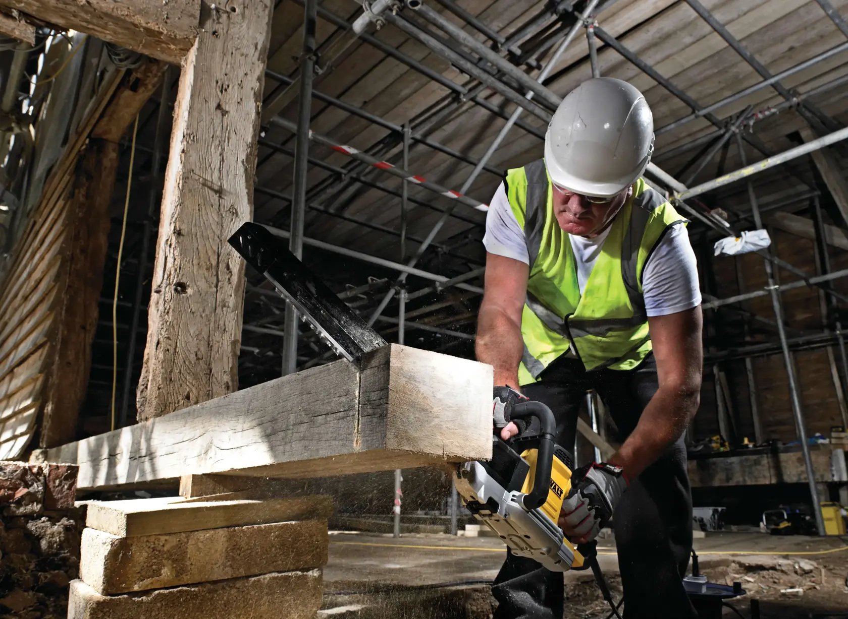 Worker uses DEWALT saw to cut wood beam at a construction site, wearing safety gear and a hi-vis vest.