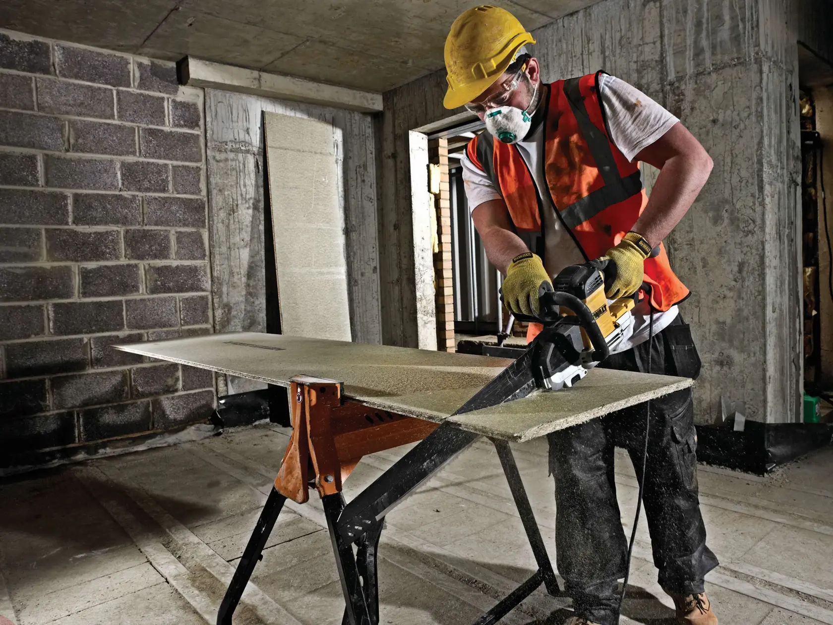 Worker uses DEWALT saw to cut a board on a worksite, wearing safety gear and protective equipment.