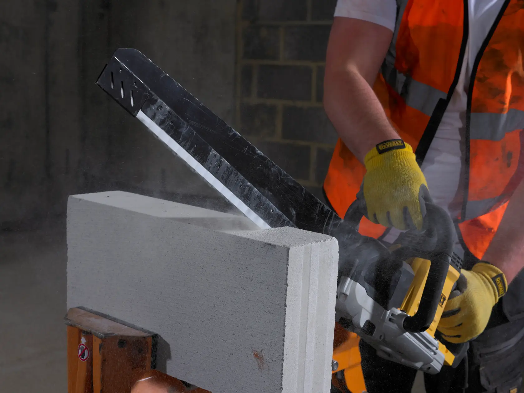 Worker uses DEWALT saw to cut concrete block, wearing gloves and safety vest.