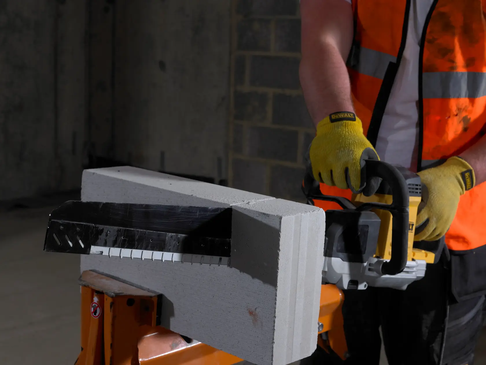 Person using a DEWALT saw with gloves to cut a concrete block indoors.