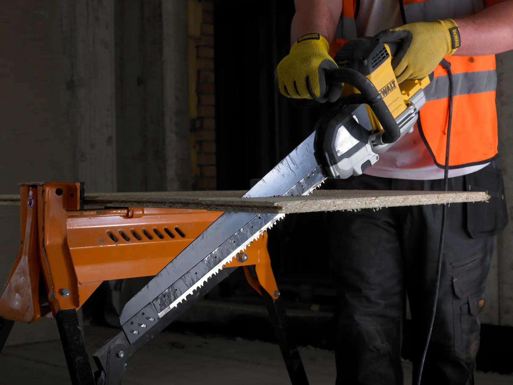 Person cuts wood with a DEWALT electric saw, wearing gloves and safety vest, wood supported by an orange workbench.