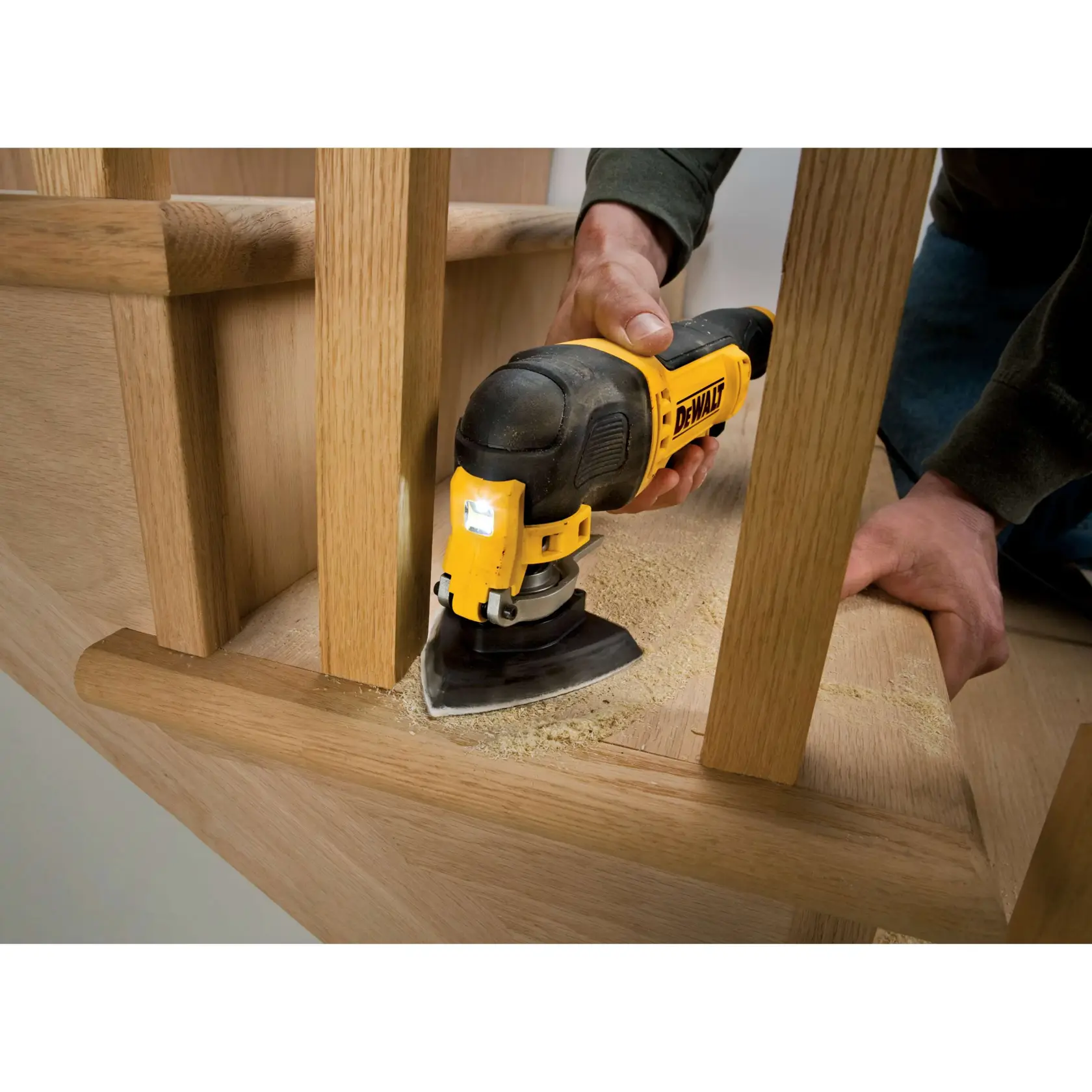 A DEWALT multi-tool is sanding wood stairs, operated by hand, with visible wood dust.