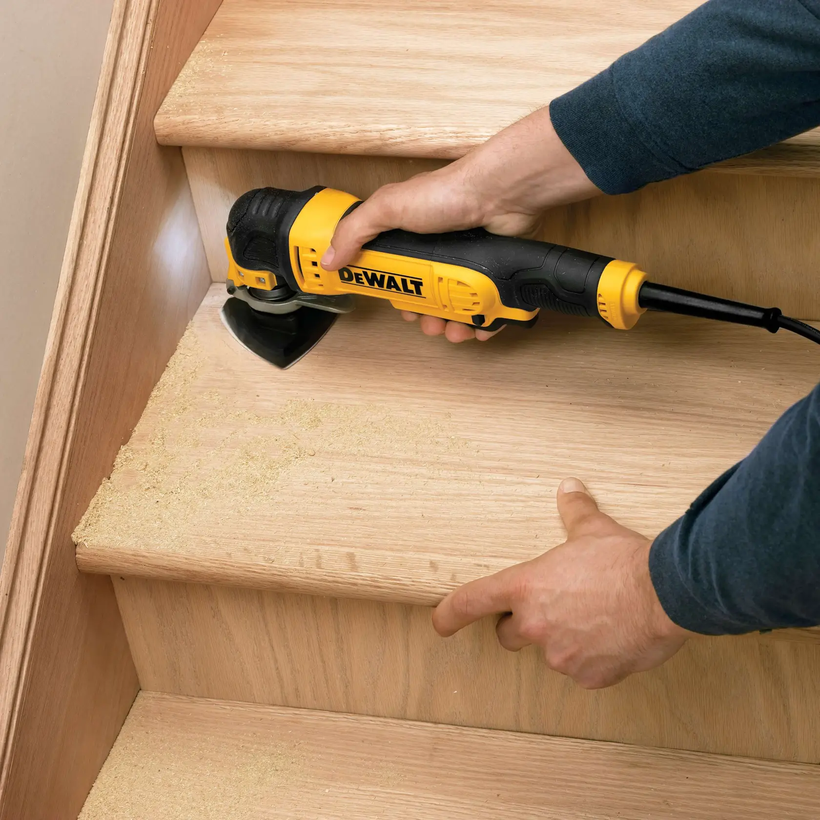 A DEWALT DT3093 tool is sanding a wooden stair, creating fine dust on the steps.