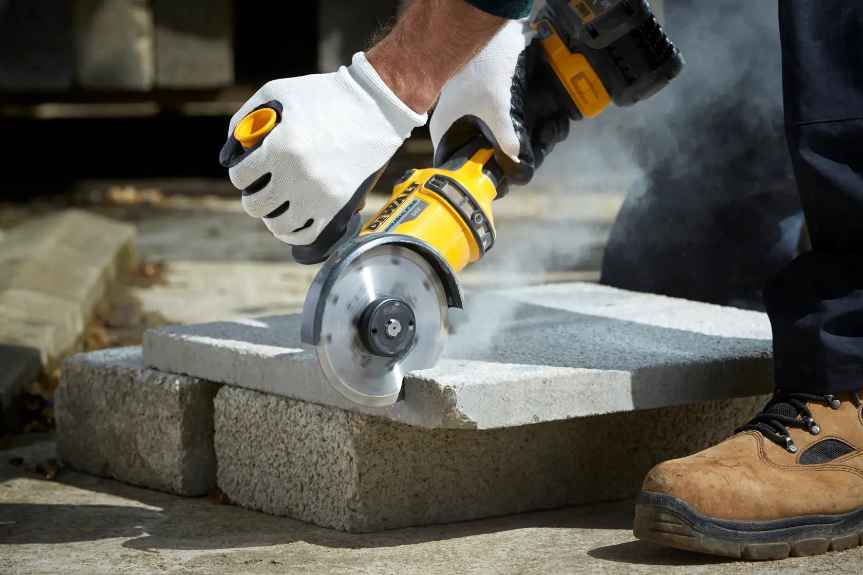 Person cuts concrete block with DEWALT angle grinder, wearing gloves and boots, dust visible.