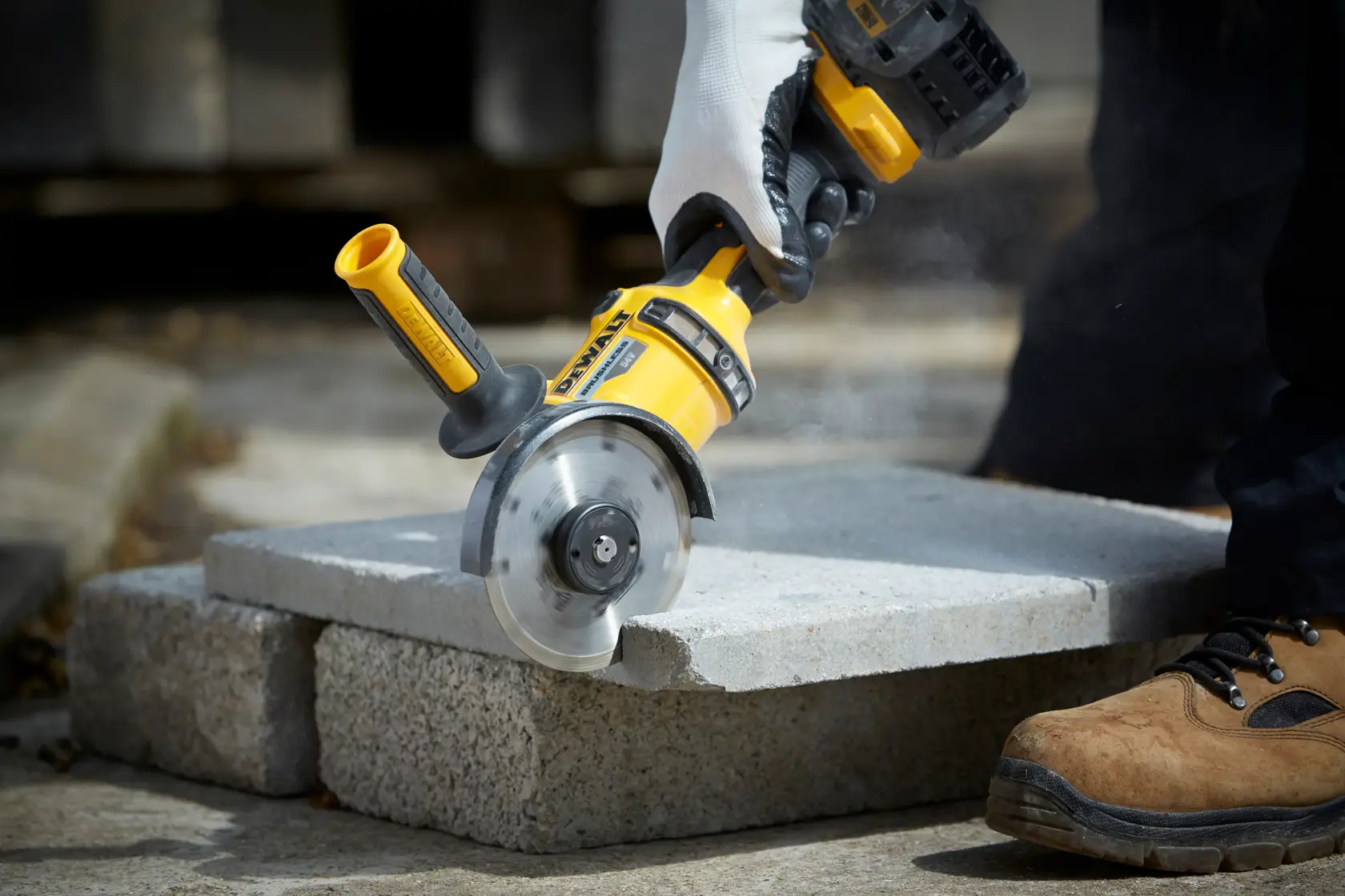 DEWALT grinder cutting concrete slab outdoors, operated by gloved hand and worker in brown safety boots.