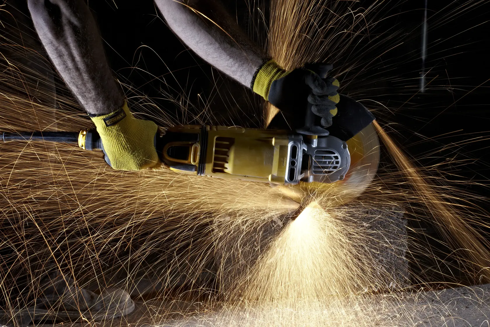 A person uses a DEWALT angle grinder, producing bright sparks while cutting material, wearing protective gloves.