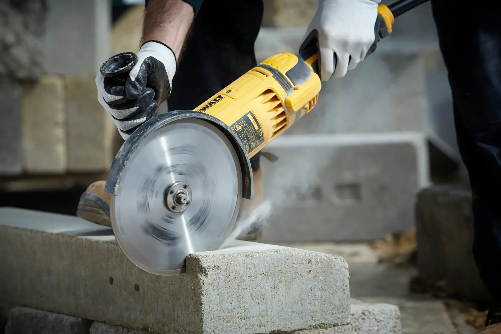 Person cutting a concrete block with a yellow DEWALT power tool, wearing gloves for safety.