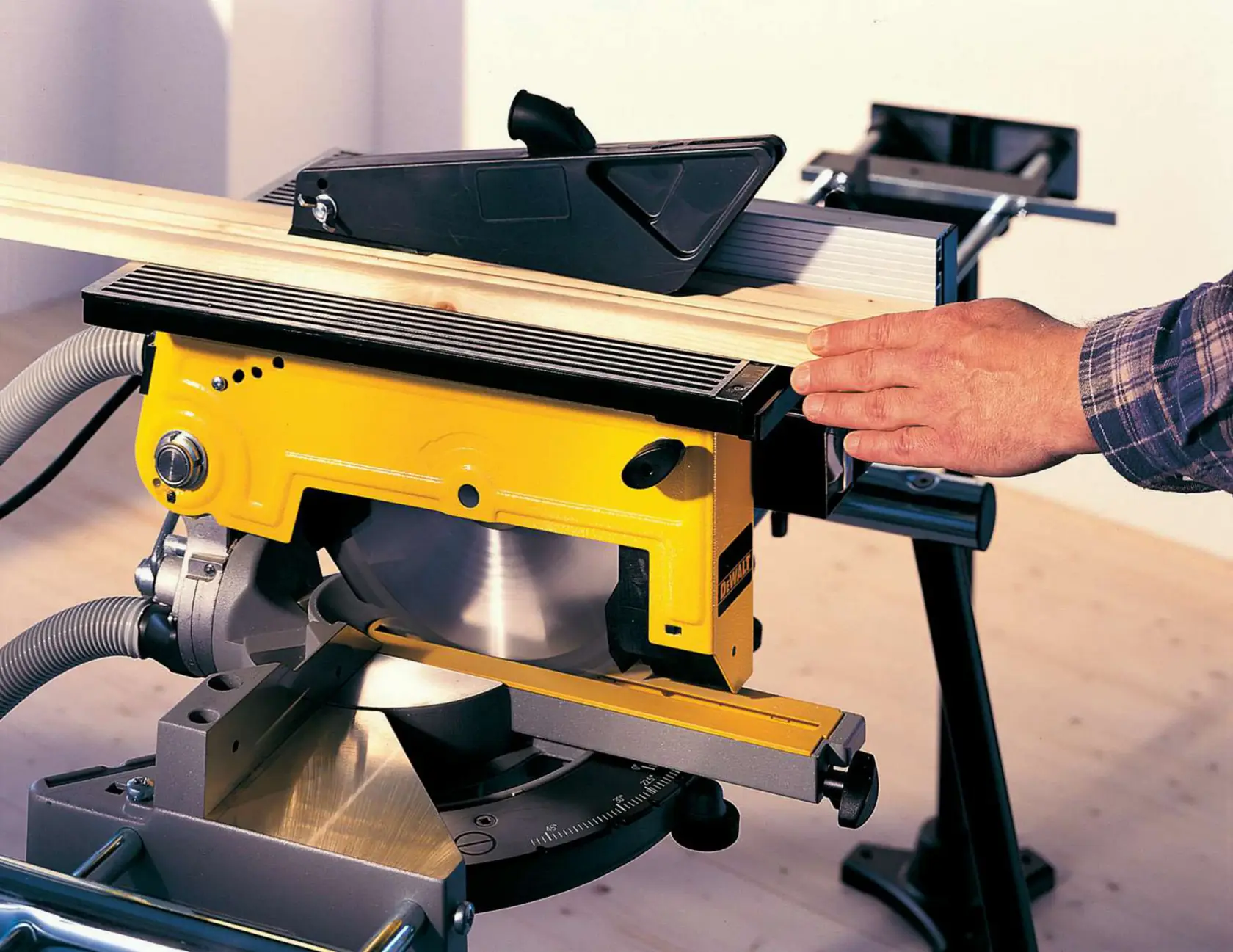 DEWALT table saw with yellow body shown in use, cutting wood on a workbench indoors.