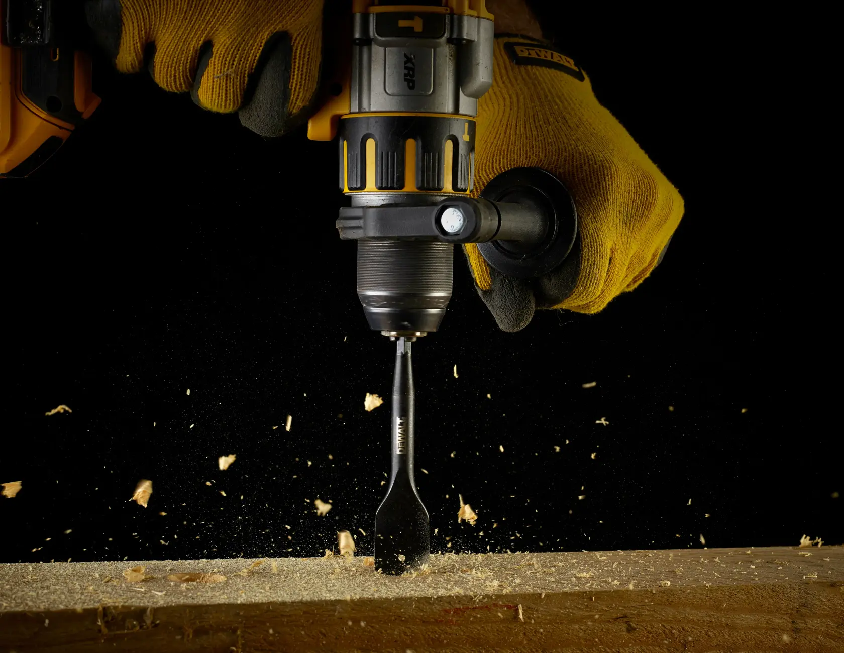 DEWALT drill in use with gloves, drilling wood and creating sawdust, shown against a black background.