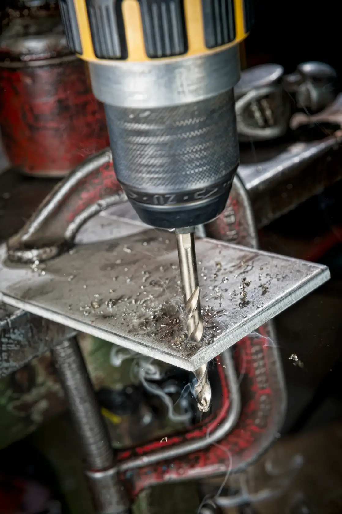 A drill with a DEWALT bit making a hole in a clamped metal sheet, with metal shavings visible.