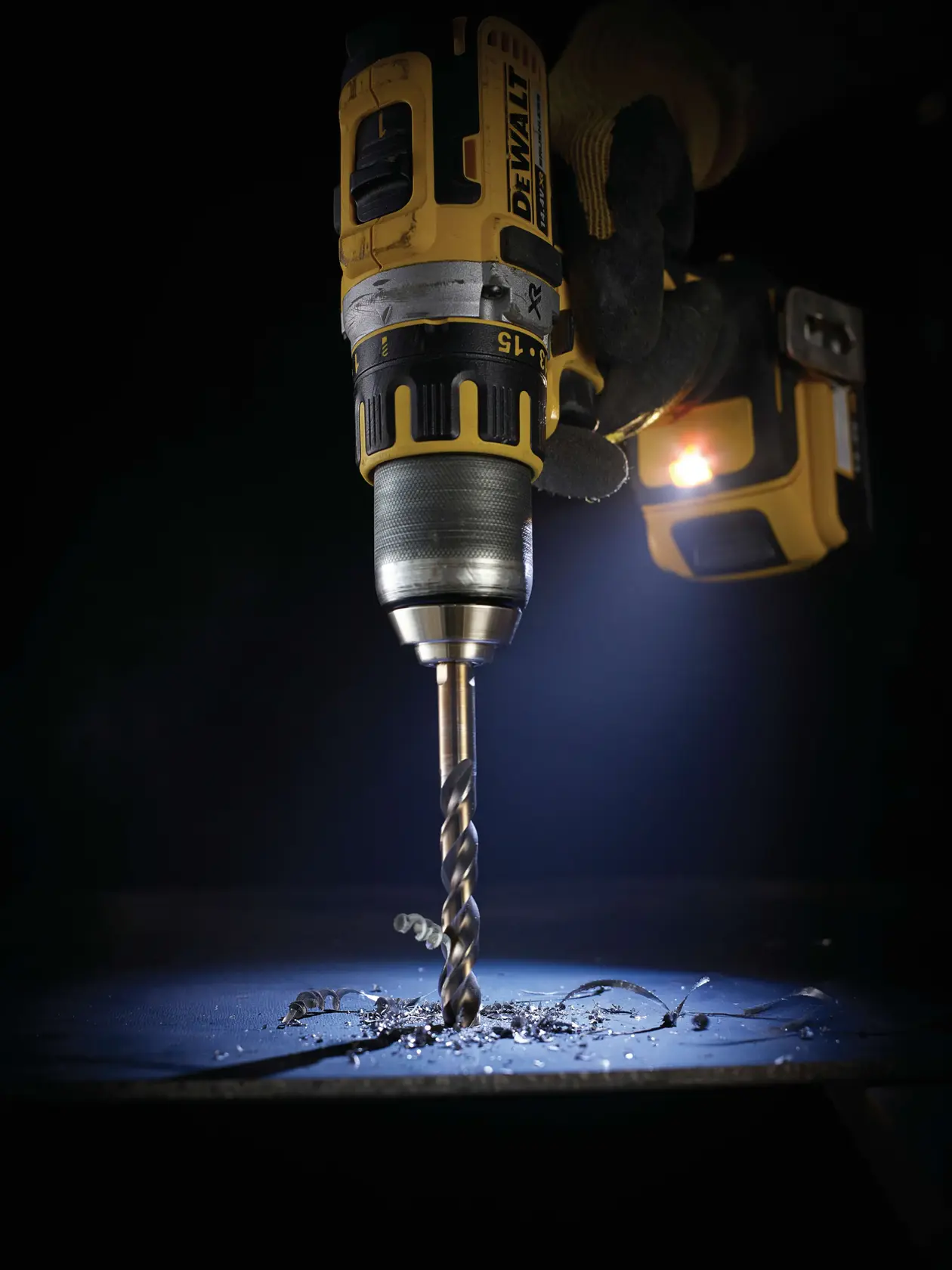 A DEWALT drill in use, drilling into metal with visible shavings and illuminated by a built-in LED light.