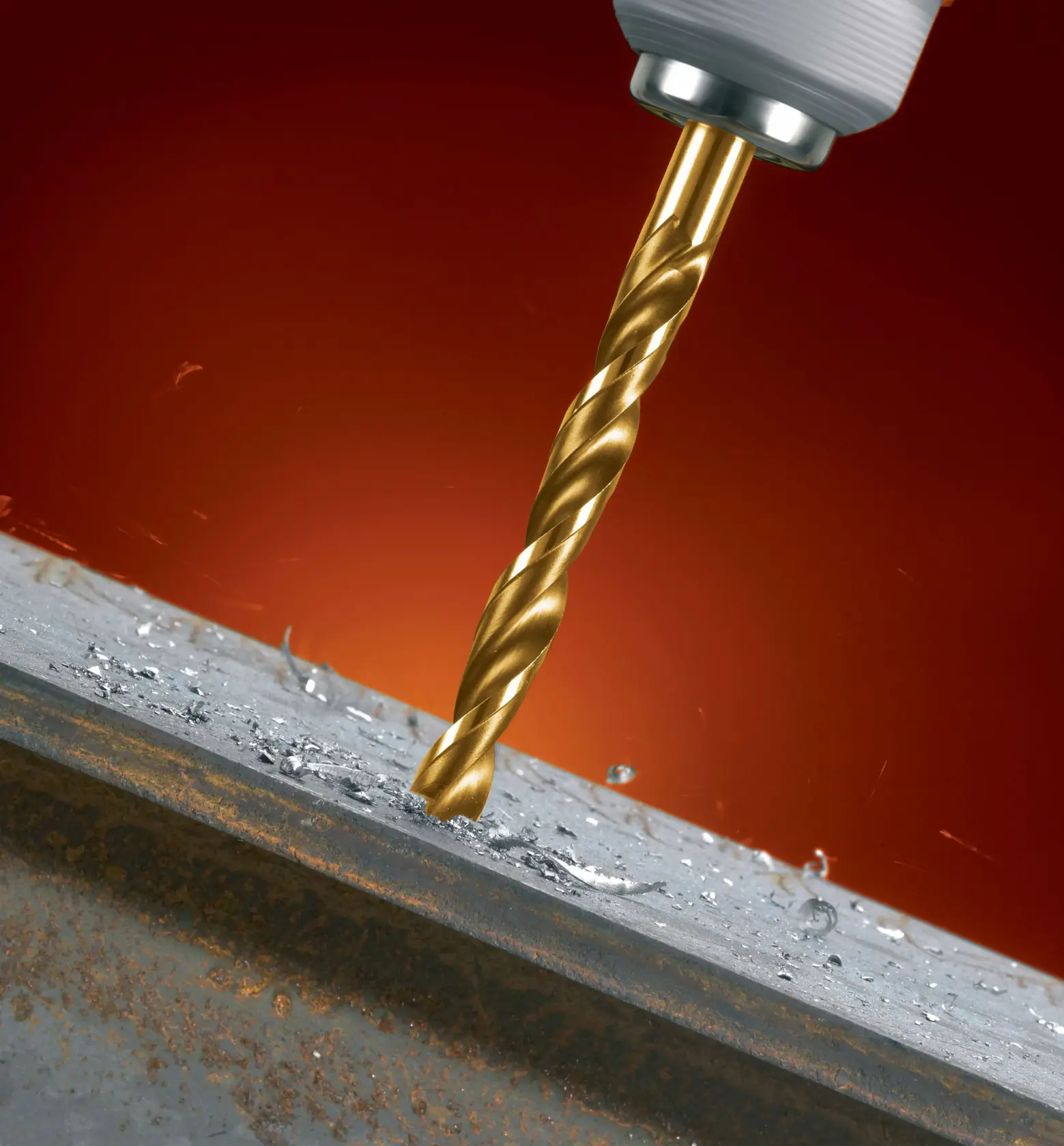 Close-up of a gold-colored drill bit drilling into a metal surface, with metal shavings around the hole.