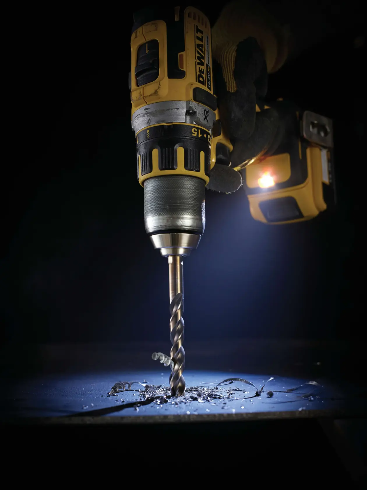 Close-up of a DEWALT drill making a hole in metal, with shavings and dark background.