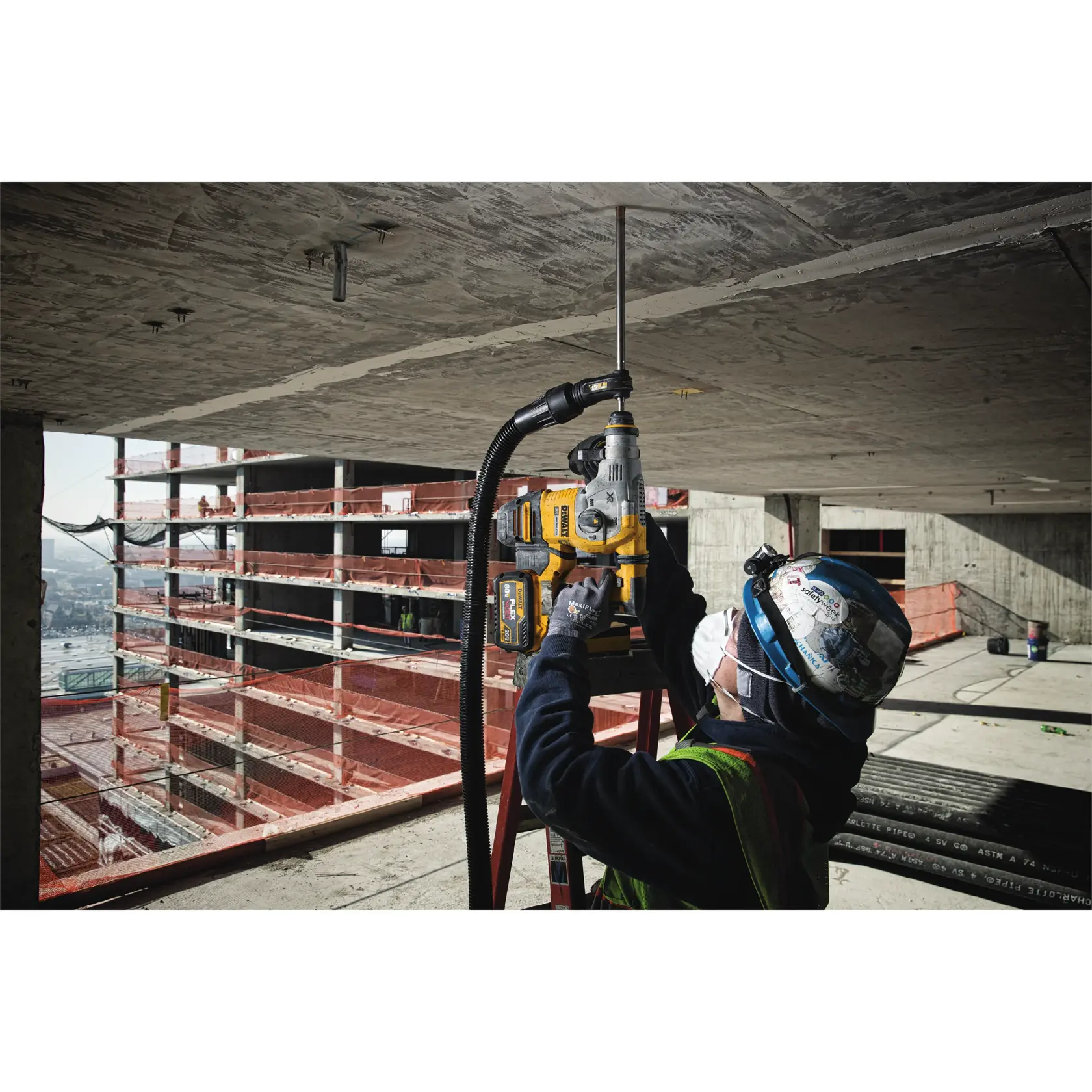 Worker drills into ceiling with DEWALT tool at a construction site, wearing helmet and mask for safety.