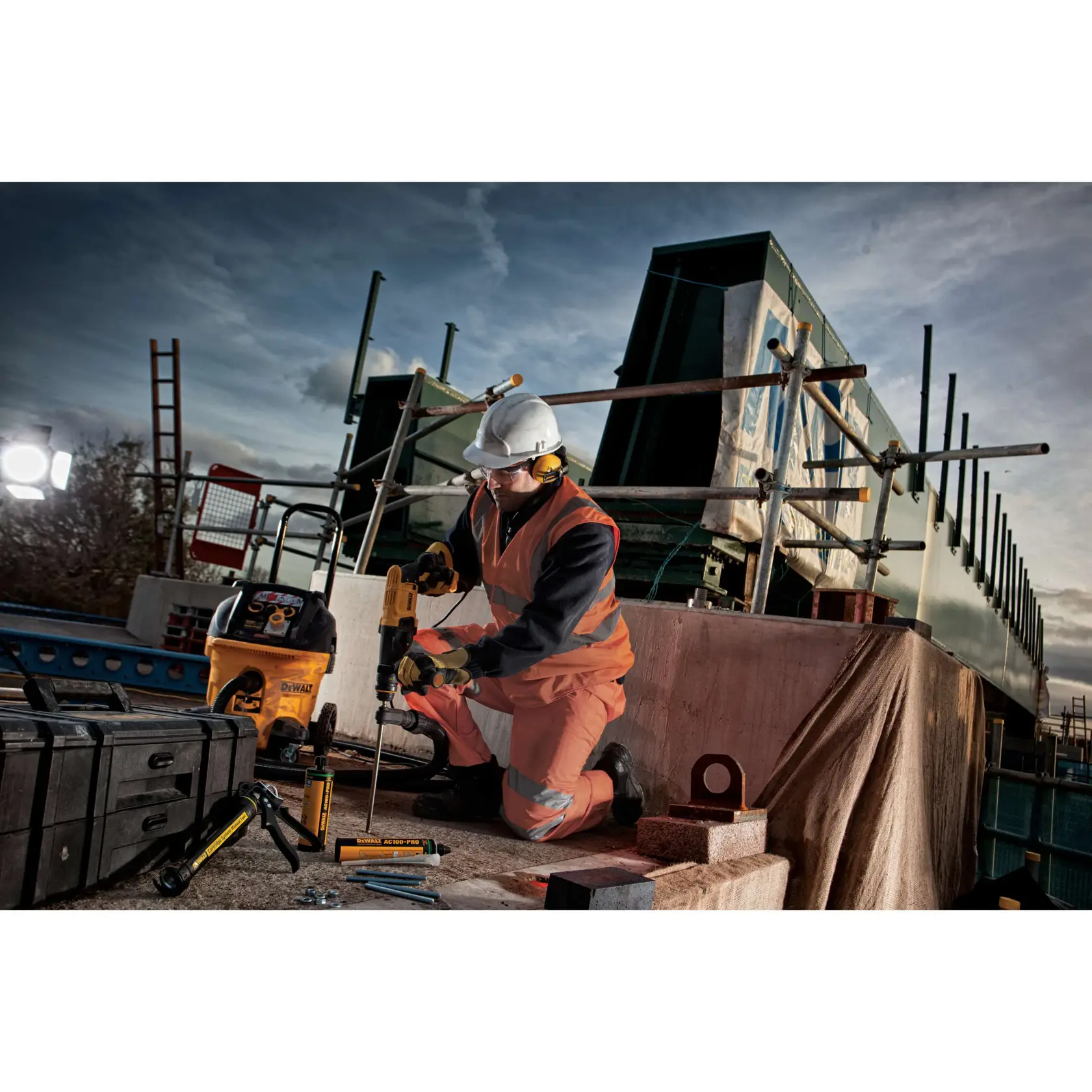 Worker using DEWALT drill on a construction site, wearing safety gear and surrounded by DEWALT tools and equipment.