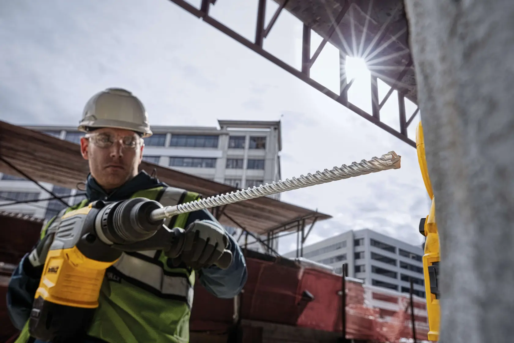 Worker holding DEWALT DT60810 drill bit at a construction site with buildings in the background.