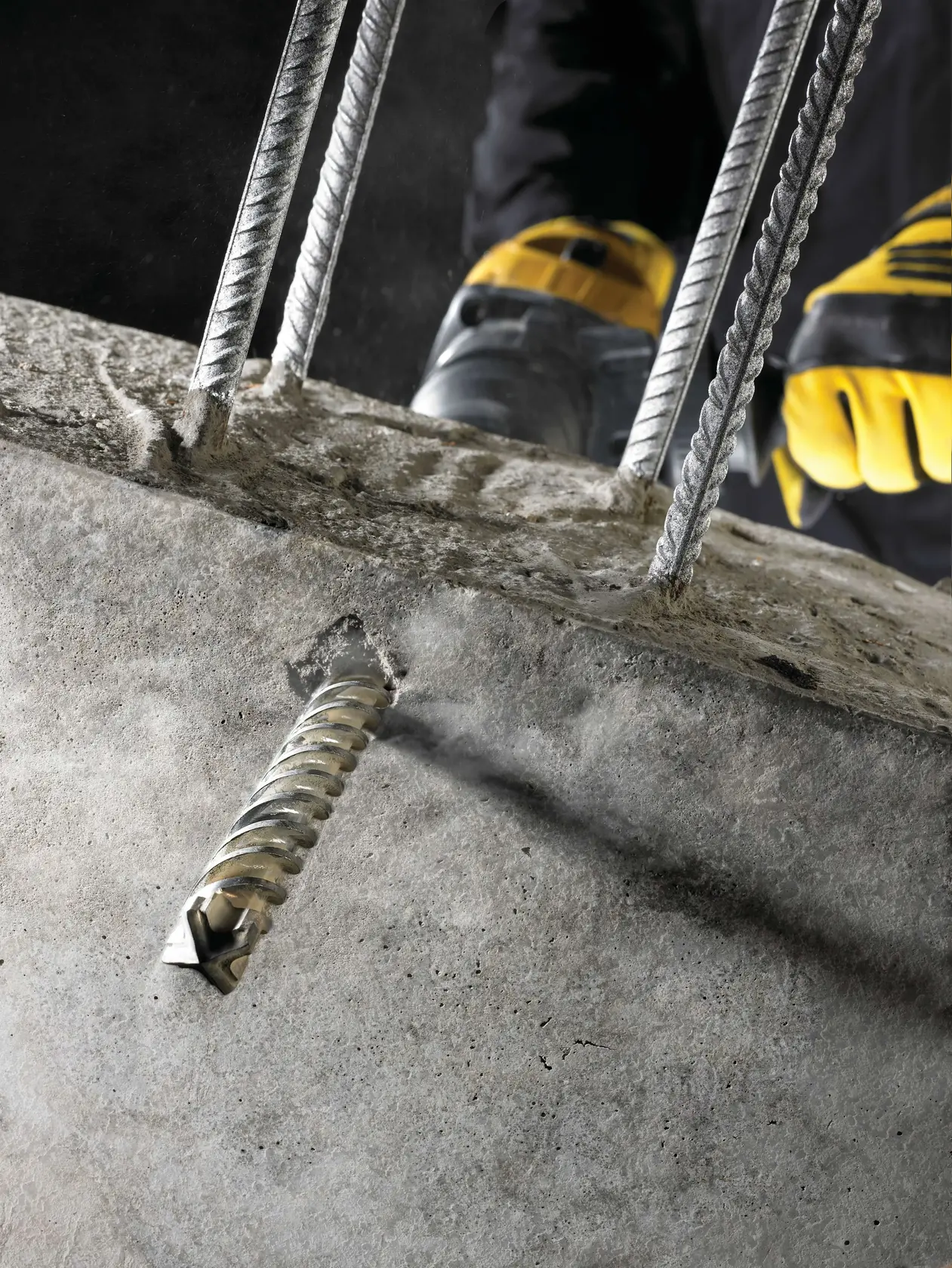 DEWALT drill bit boring through concrete with steel rebars, operated by worker wearing yellow gloves.