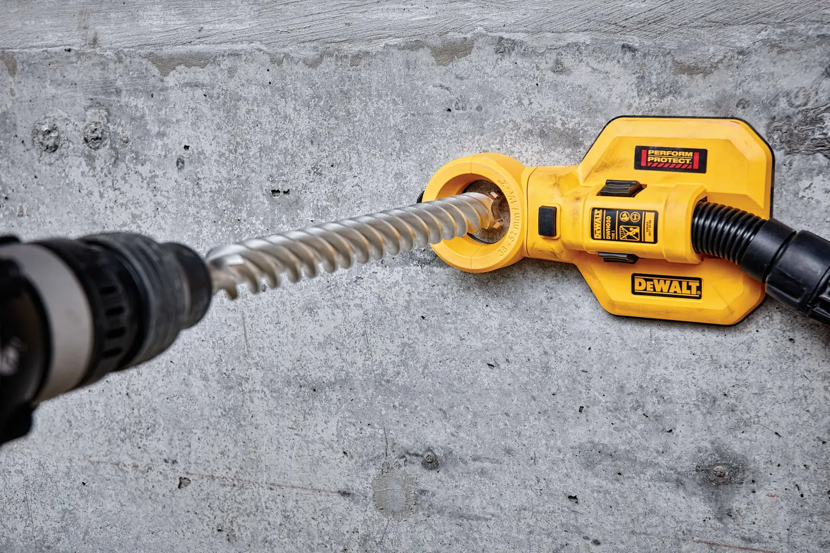 DEWALT tool attachment used on concrete wall with a drill and vacuum hose for dust extraction.
