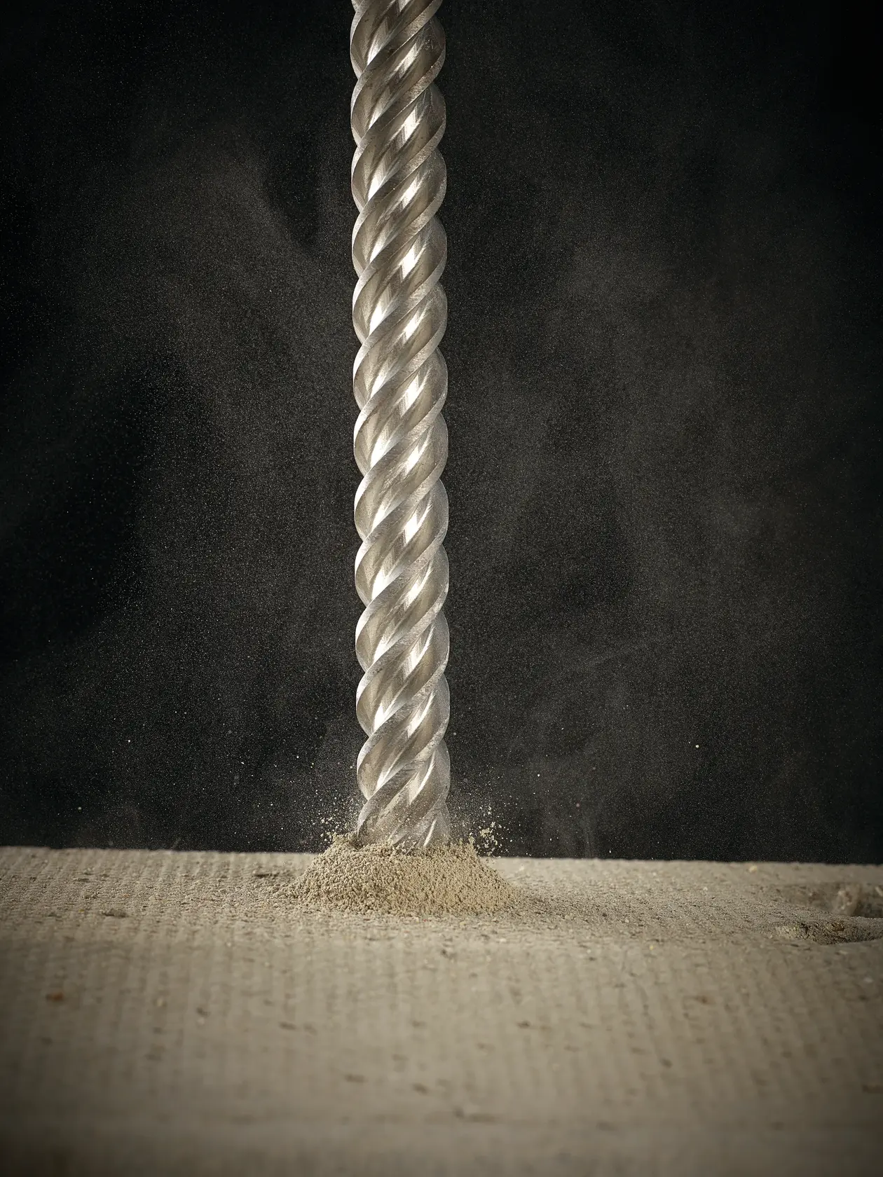 Close-up of a DEWALT drill bit penetrating a concrete surface, producing dust and debris.